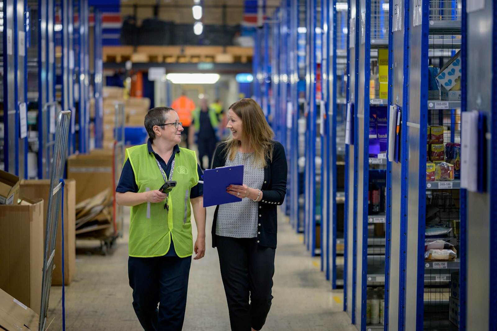 Twee collega’s lopen in gesprek door een magazijn